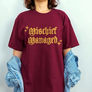 May include: Burgundy t-shirt with the text "Mischief Managed" in gold lettering with stars on either side.