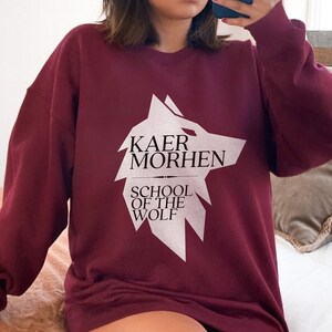 May include: A maroon sweatshirt with a white wolf graphic and the text "Kaer Morhen School of the Wolf".