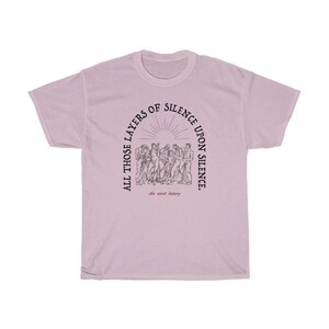 May include: A light pink t-shirt with a black graphic print of a group of people standing in a circle. The text around the circle reads "All those layers of silence upon silence." The text below the circle reads "the secret history."