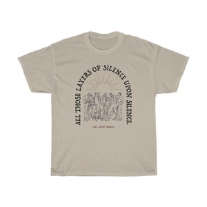 May include: A beige t-shirt with a black graphic print of a group of people standing in a circle. The text around the graphic reads "All those layers of silence upon silence -the secret history-."