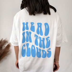 Peut inclure: T-shirt blanc avec un graphisme bleu qui dit "HEAD IN THE CLOUDS" dans une police rétro.