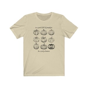 May include: A cream-coloured t-shirt with a black and white pumpkin illustration. The text reads "in a patch full of pumpkins" and "be a jack-o-lantern" above and below the pumpkin graphic.