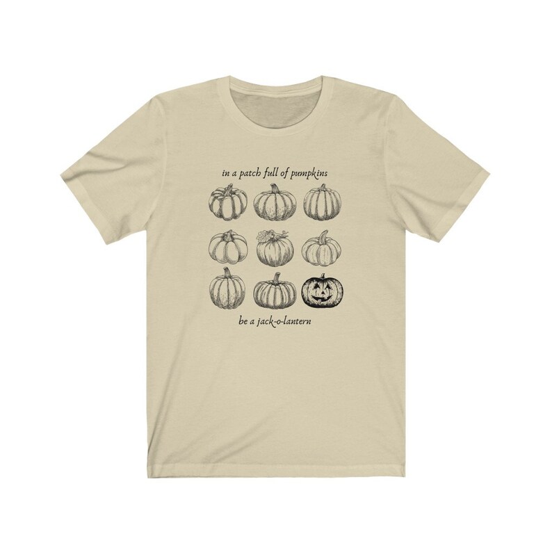 May include: A cream-coloured t-shirt with a black and white pumpkin illustration. The text reads "in a patch full of pumpkins" and "be a jack-o-lantern" above and below the pumpkin graphic.