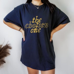 May include: A navy blue oversized t-shirt with a gold graphic that says "the chosen one" in a retro font.