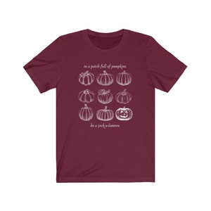 May include: A maroon t-shirt with a white graphic of nine pumpkins, including a jack-o'-lantern. The text "in a patch full of pumpkins" and "be a jack-o-lantern" are above and below the pumpkin graphic.
