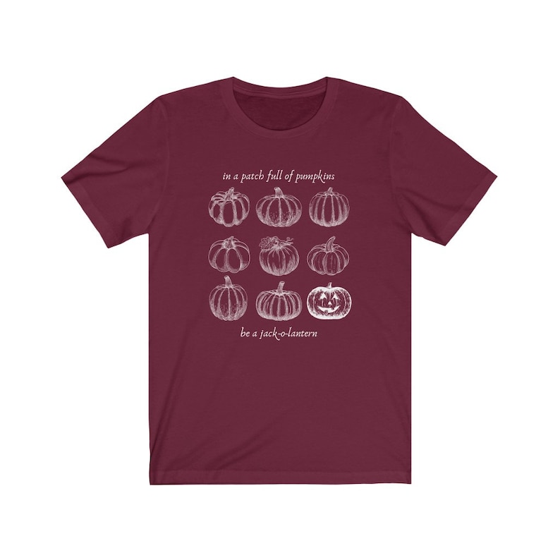 May include: A maroon t-shirt with a white graphic of nine pumpkins, including a jack-o'-lantern. The text "in a patch full of pumpkins" and "be a jack-o-lantern" are above and below the pumpkin graphic.