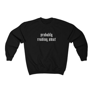 Puede incluir: Sudadera negra con la frase blanca "probably reading smut" en fuente g&oacute;tica. Esta prenda informal de cuello redondo est&aacute; dise&ntilde;ada para la comodidad y el uso diario. El texto est&aacute; centrado en el pecho.