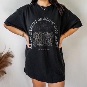May include: Black oversized t-shirt with a graphic print of a group of people standing in front of a sunburst. The text reads "All those layers of silence upon silence - the secret history -"