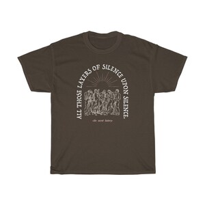 May include: A brown t-shirt with a white graphic print of a group of people standing in a circle. The text reads "All those layers of silence upon silence -the secret history-."