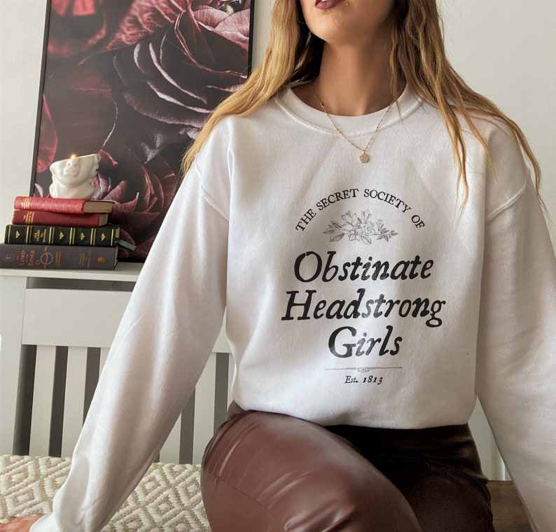 May include: White sweatshirt with black text that reads "The Secret Society of Obstinate Headstrong Girls Est. 1913".