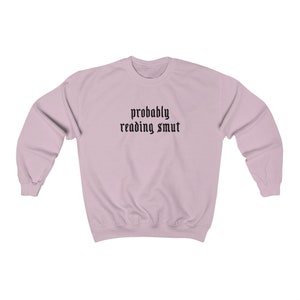 Puede incluir: Sudadera rosa claro con la frase "probably reading smut" impresa en negro con fuente g&oacute;tica. La sudadera tiene mangas largas y cuello redondo.