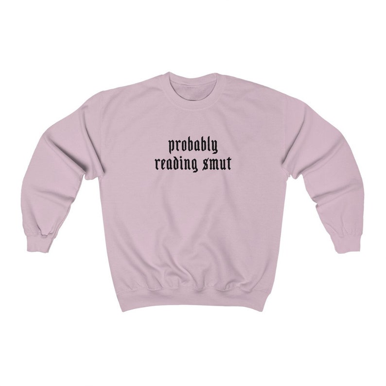 Puede incluir: Sudadera rosa claro con la frase "probably reading smut" impresa en negro con fuente g&oacute;tica. La sudadera tiene mangas largas y cuello redondo.