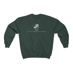May include: Dark green sweatshirt with a white graphic of a classical bust and the text "we are more beautiful because we are doomed". The sweatshirt is made of a soft material and has a crew neck.