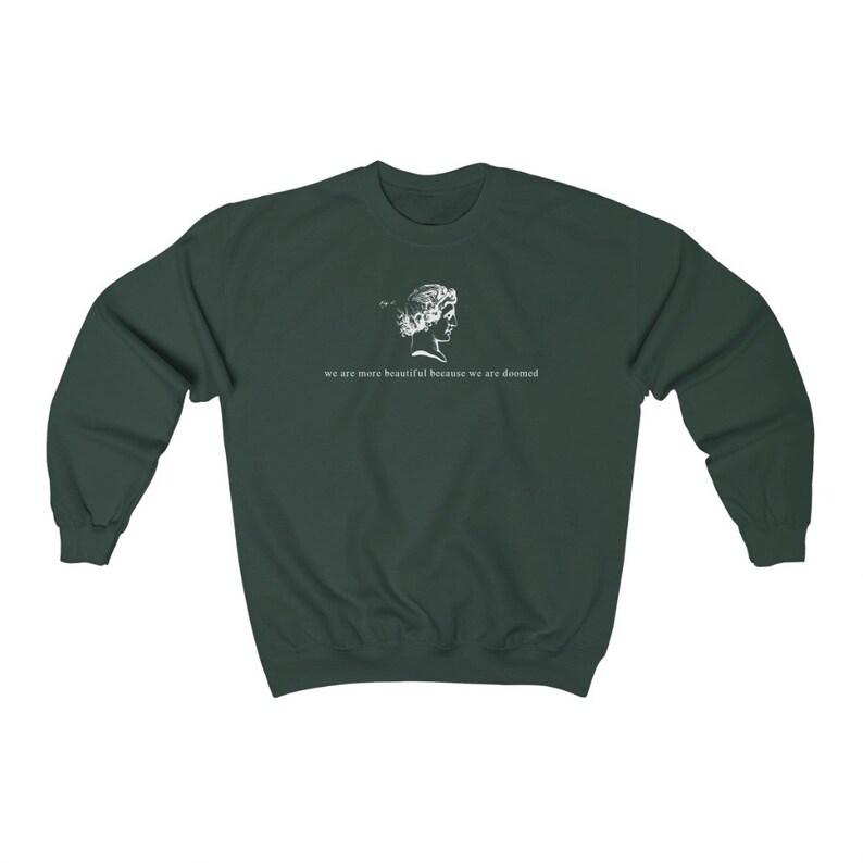 May include: Dark green sweatshirt with a white graphic of a classical bust and the text "we are more beautiful because we are doomed". The sweatshirt is made of a soft material and has a crew neck.