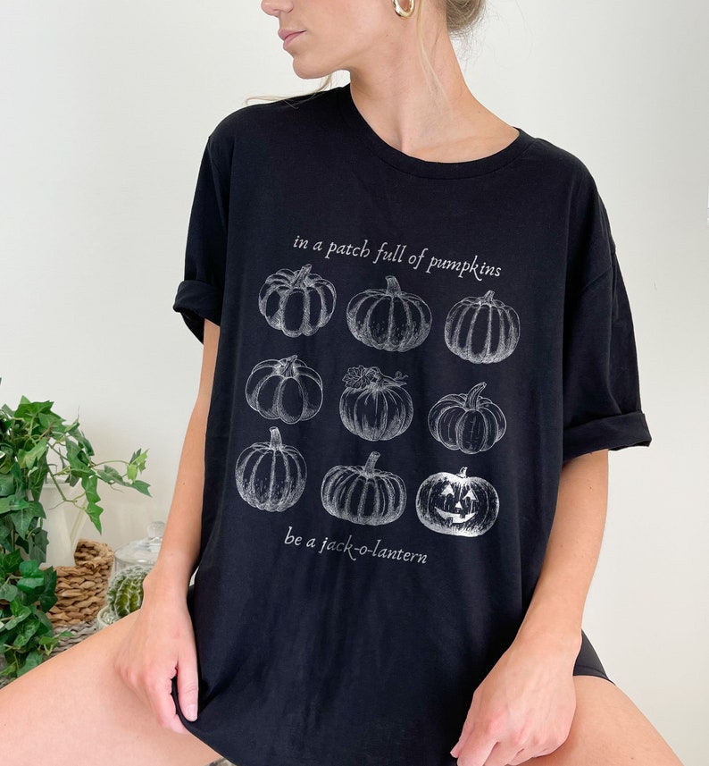 May include: Black t-shirt with a white illustration of pumpkins, including a jack-o'-lantern. The text reads "in a patch full of pumpkins" and "be a jack-o'-lantern". A casual, comfortable top for autumn.