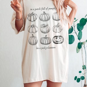 May include: Cream-coloured t-shirt with a pumpkin patch design. The shirt features a graphic of nine pumpkins, with the text "in a patch full of pumpkins" and "be a jack-o-lantern". The t-shirt has a relaxed fit.