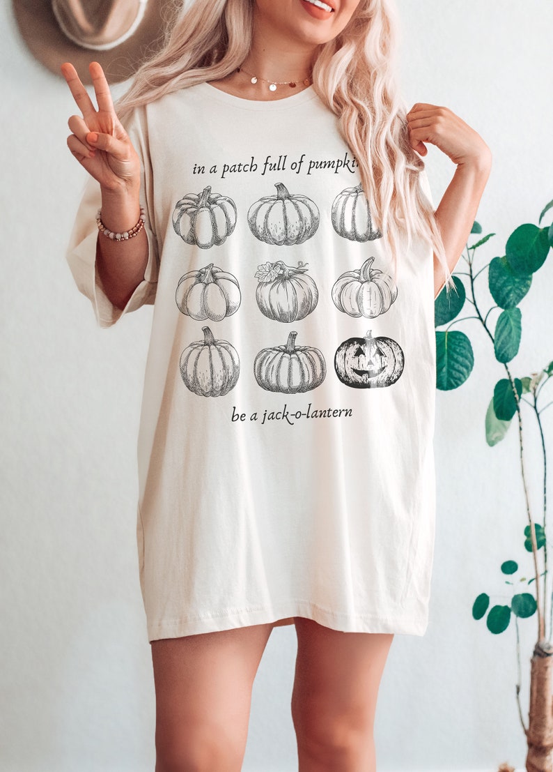 May include: Cream-coloured t-shirt with a pumpkin patch design. The shirt features a graphic of nine pumpkins, with the text "in a patch full of pumpkins" and "be a jack-o-lantern". The t-shirt has a relaxed fit.