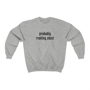Puede incluir: Sudadera gris claro con la frase "probably reading smut" en fuente g&oacute;tica negra en el pecho. La sudadera tiene mangas largas y cuello redondo.