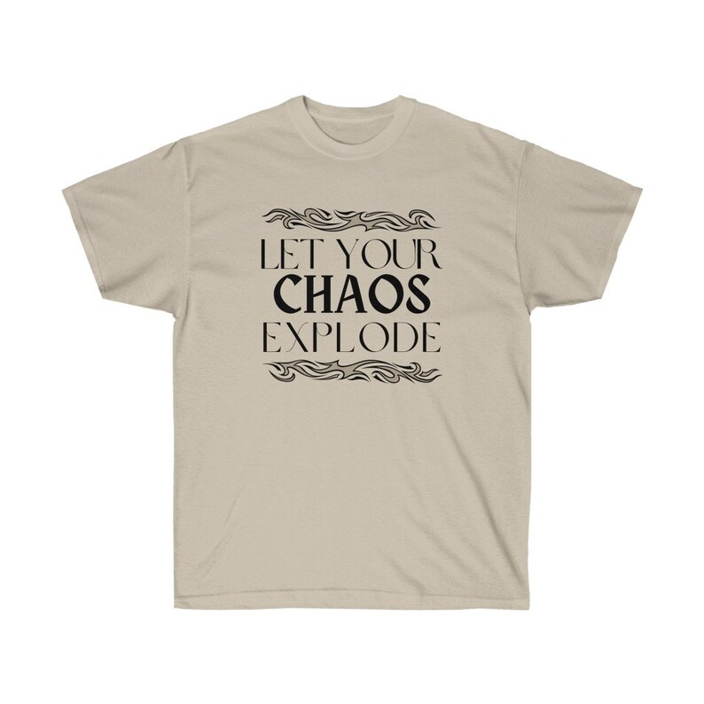 May include: A beige t-shirt featuring the black text "LET YOUR CHAOS EXPLODE", framed by decorative wavy lines. The shirt is made of a soft material. The design is centered on the front of the tee.