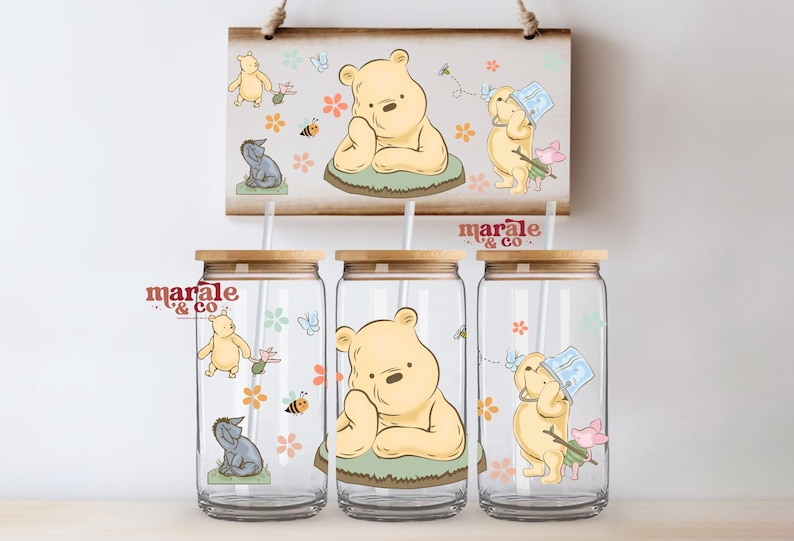 Pu&ograve; includere: Tre bicchieri di vetro con coperchi e cannucce in bamb&ugrave;, con illustrazioni di Winnie the Pooh. Il design include Winnie the Pooh, Eeyore, Pimpi, api e fiori. Un cartello di legno abbinato &egrave; appeso sopra i bicchieri.
