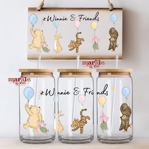 Può includere: Tre bicchieri in vetro trasparente con coperchi in bambù e cannucce bianche, ciascuno con un'illustrazione di Winnie the Pooh e i suoi amici che tengono palloncini, con la scritta Winnie & Friends sopra una targa in legno abbinata.