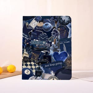 May include: A navy blue collage notebook featuring various images and text, including a watch, a blueberry, a car, and the phrase "just keep going." The design incorporates a heart shape and a disco ball.