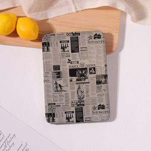 May include: Rectangular coaster with a newspaper print design. The coaster features various headlines, articles, and the words "DAILY NEWS" and "HOROSCOPES". The coaster is on a wooden surface with two lemons.