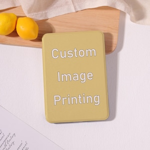 May include: A rectangular, mustard-yellow electronic device with rounded corners. The front surface features the white text "Custom Image Printing" centered in a clean, sans-serif font. The device has a smooth, matte finish.
