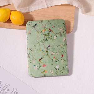 May include: A rectangular, pale green case with a floral and bird design. The case features a pattern of flowering branches, birds, and small pagodas. The design is in shades of green, pink, and white.