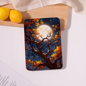 May include: A rectangular protective case for an electronic device featuring a dark night sky illustration with a large, bright full moon and a tree with vibrant orange and yellow autumn leaves silhouetted against the starry background.