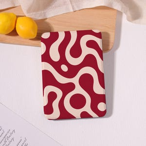 May include: A rectangular, red and cream-colored patterned object. The design features a series of interconnected, swirling shapes in cream against a red background. Two yellow lemons rest on a wooden surface nearby.