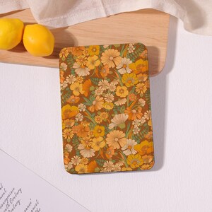 May include: A rectangular tablet case featuring a dense, repeating floral pattern in shades of mustard yellow, burnt orange, cream, and sage green against a dark brown background, with rounded corners and a smooth, flat surface.