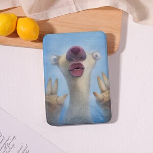 May include: A blue tablet case featuring a cartoon sloth character with a large pink nose and lips. The sloth is making a peace sign with its fingers. The background is a light blue color.