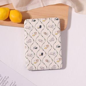 May include: Rectangular cream-colored notebook with a repeating pattern of reading animals and green vines. The animals include rabbits, cats, and pandas. Two yellow lemons are visible in the upper left corner.
