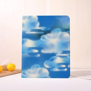 May include: A rectangular notebook with a blue sky and cloud design. The cover features a vibrant illustration of fluffy white clouds against a bright blue background. The notebook is a perfect accessory for writing and note-taking.