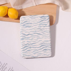 May include: A rectangular electronic reader case featuring a light blue and white wavy zebra-like pattern. The case has rounded corners and a smooth, flat surface, displaying a consistent horizontal ripple design across the entire front cover.