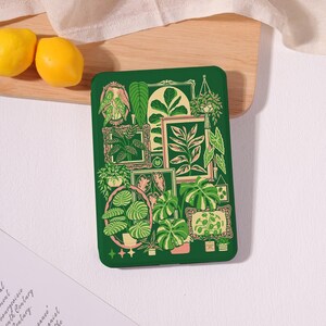 May include: A green phone case featuring a botanical illustration. The design includes various framed plant illustrations in shades of green, beige, and pink. Two yellow lemons are visible in the background.