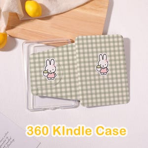 May include: A 360 Kindle case featuring a light sage green and white gingham check pattern. The front cover displays a small illustration of a white rabbit wearing a pink dress and holding a green cup. The case includes a clear plastic shell.