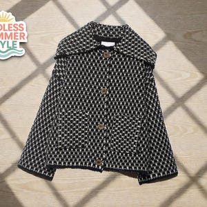 Könnte beinhalten: Schwarz-weiß gemusterte Jacke mit Kragen und Holzknöpfen. Die Jacke hat ein geometrisches Design und wird auf einer Holzoberfläche präsentiert. Das Bild enthält einen Aufkleber mit der Aufschrift "ENDLESS SUMMER STYLE".