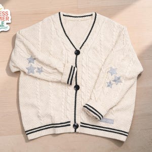 May include: Cream cable knit cardigan with black trim and buttons. Light blue star embroidery adorns the sleeves. The text "ENDLESS SUMMER STYLE" is on a sticker in the upper left corner.