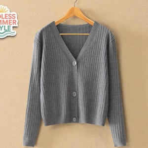 May include: A gray, ribbed-knit cardigan with a V-neck and three buttons. The long-sleeved sweater is hanging on a wooden hanger against a neutral background. A sticker in the upper left corner reads "ENDLESS SUMMER STYLE".