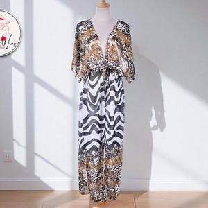 May include: A long, flowing jumpsuit with a V-neck and wide legs. The top features a leopard print, while the bottom has a black and white zebra pattern. The garment is displayed on a mannequin. The Waves & Wrap Boutique logo is in the upper left corner.
