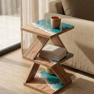 May include: A three-tiered wooden side table with a unique design. The table features a turquoise and white wave design on each shelf. A small, brown ceramic cup sits on the top shelf. Books and a woven basket are on the middle and bottom shelves.
