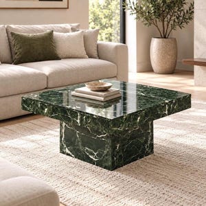 May include: A square coffee table crafted from dark green marble with prominent white veining. The table features a thick, flat top surface supported by a matching solid block base. A small, shallow stone bowl sits atop two stacked books.