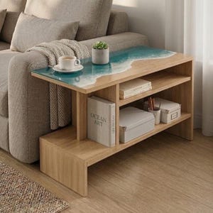 May include: A light wood side table featuring a rectangular top with a blue and white resin ocean wave design. The table includes two open storage shelves containing books, a white box, and a small succulent plant in a grey pot.