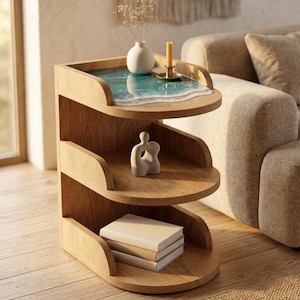 May include: A three-tiered wooden side table with a unique design. The top shelf features a resin art piece depicting an ocean scene. The middle shelf holds a small sculpture, and the bottom shelf displays a stack of books. A vase, candle, and dried flowers are on the top shelf.