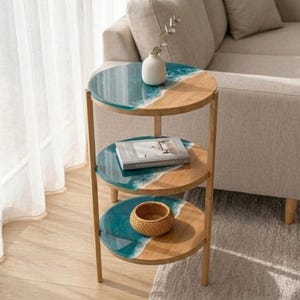 May include: A three-tiered side table with a unique design. Each round tier features a teal resin section resembling water, and a light wood section. A small white vase and a woven basket are on the table.