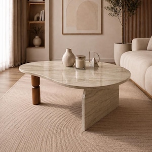 May include: A coffee table with an irregular, kidney-shaped top made of polished beige stone with natural veining. The table is supported by one cylindrical dark wood leg and one solid, flat, stone-textured panel base in a matching beige tone.