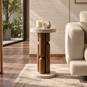 May include: A round side table featuring a light-coloured speckled stone top and base connected by four vertical dark brown wooden cylindrical supports. A clear glass candle holder with a white wax candle and a geometric stone object sit on top.