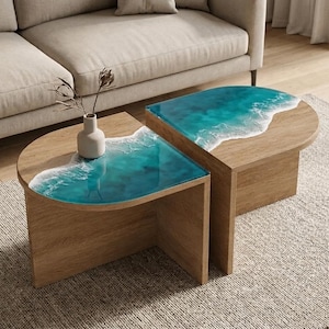 May include: Two semi-circular wooden coffee tables featuring a blue and white resin inlay that mimics ocean waves. The tables have a light wood grain finish and are positioned together to form a larger surface. A small white vase sits on one table.